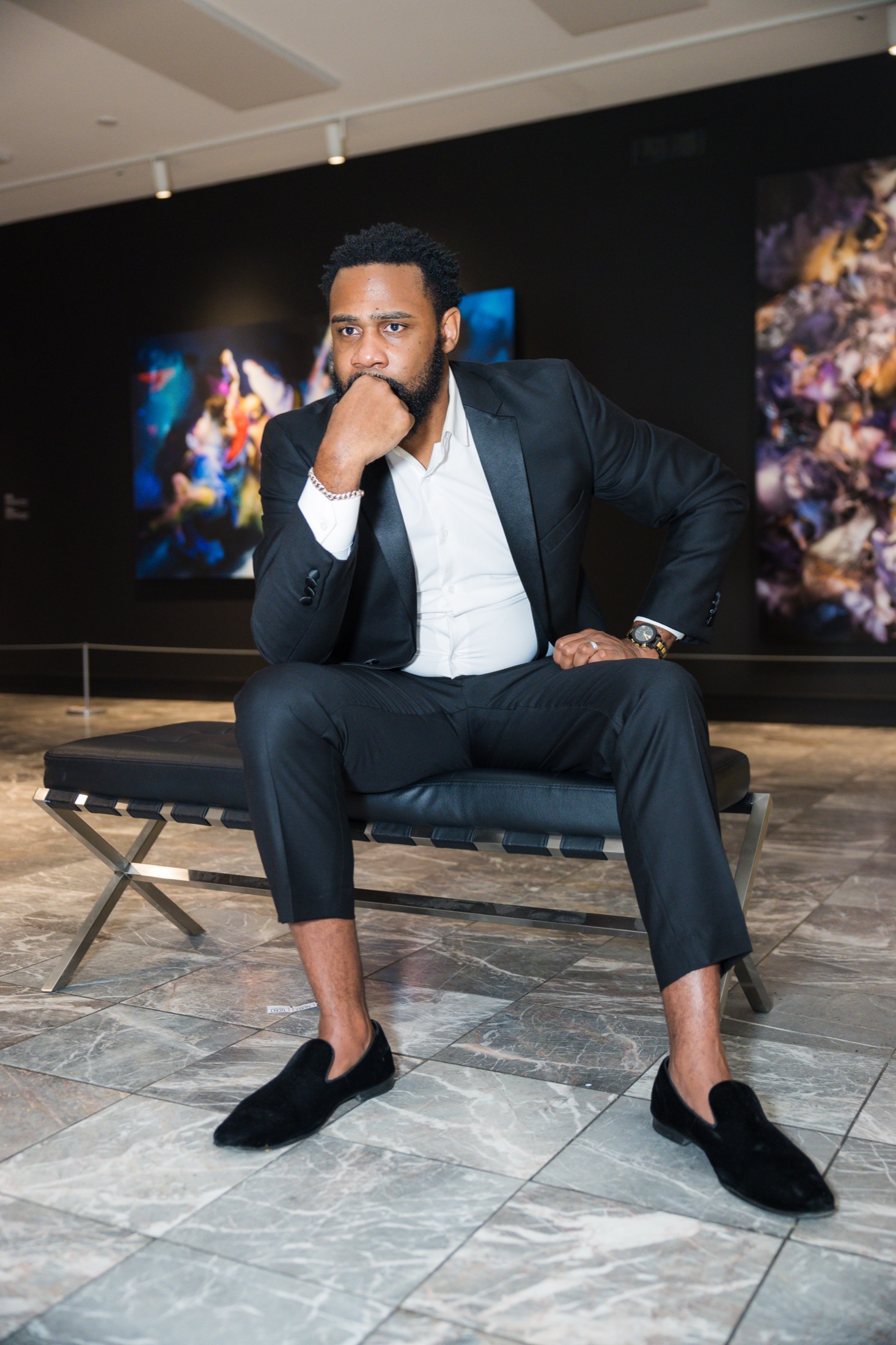 Rodriquez Wright II seated in a dark gallery, wearing a black suit